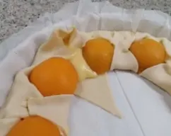 Step <p>Vamos ajustando los cortes al melocotón para cerrar la masa.</p><p>Pintamos la masa con huevo batido y repartimos las almendras laminadas.</p><p>Pintamos de nuevo con huevo batido y espolvoreamos con azúcar.</p> illustration