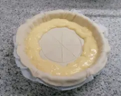 Step <p>Preparamos nuestra fuente de horno y extendemos la hoja de hojaldre.</p><p>Hacemos sin cortar un circulo en el centro de la masa,y hacemos 4 cortes para hacer 8 triángulos.</p><p>Repartimos con una manga pastelera,la crema por el borde de la masa.</p> illustration